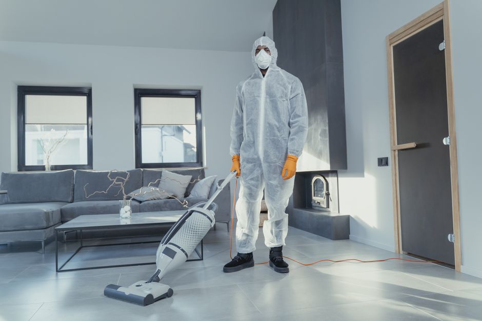 A person in protective coveralls vacuuming a contemporary living room.